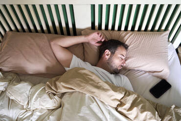 Mid adult man sleeping by mobile phone in bed - VEGF04521