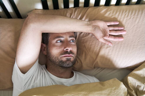Thoughtful man looking away while resting in bed - VEGF04523