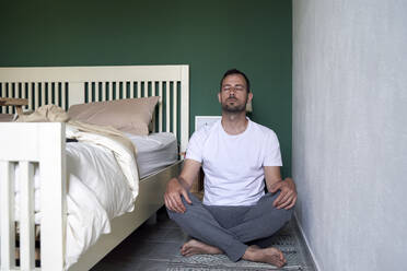 Mittlerer erwachsener Mann meditiert zu Hause sitzend - VEGF04554