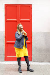 Smiling woman standing with juice in front red door - IFRF00702