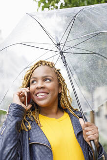 Lächelnde Frau, die mit einem Regenschirm telefoniert - IFRF00716