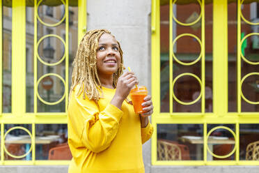 Smiling woman holding juice while looking up and day dreaming - IFRF00717