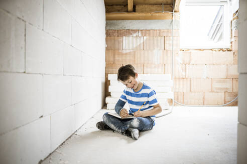 Smiling boy writing in book while sitting at attic during rebuilding - HMEF01225