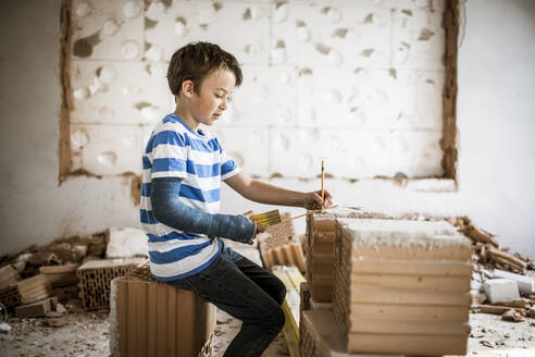 Boy measuring brick with pocket rule during rebuilding house - HMEF01228