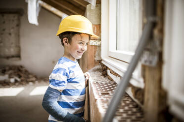 Junge mit Schutzhelm schaut durch ein Fenster auf einer Baustelle - HMEF01230