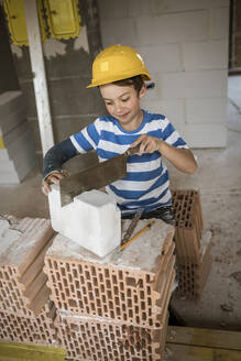 Boy with broken arm cutting block during rebuilding house - HMEF01232