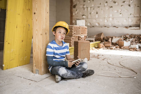 Thoughtful boy with book while sitting at construction site - HMEF01235