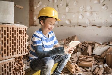 Lächelnder Junge mit Buch, der bei der Renovierung eines Hauses sitzt - HMEF01236