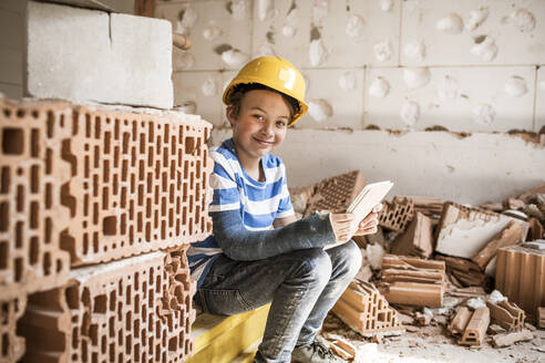 Smiling boy sitting with book at attic during renovation - HMEF01237