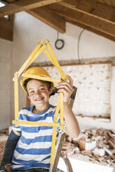 Junge, der beim Wiederaufbau eines Hauses mit dem Zollstock ein Haus formt - HMEF01241