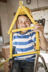 Junge hält Haus der Taschenregel am Haus während der Renovierung - HMEF01242