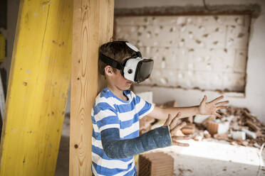 Junge mit Virtual-Reality-Headset streckt seine Hand bei der Dachbodenrenovierung aus - HMEF01249