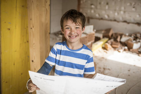 Smiling boy holding blueprint while standing at loft apartment - HMEF01250