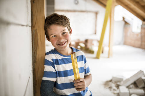 Smiling boy holding pocket rule during house renovation - HMEF01252