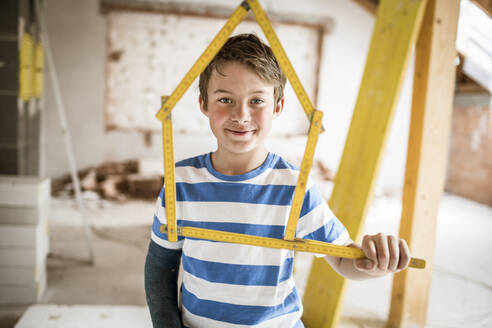 Lächelnder Junge, der ein Taschenregelwerk mit Hausform auf dem Dachboden hält - HMEF01253