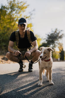 Männlicher Wanderer, der den Hund ansieht, während er auf dem Fußweg hockt - ACPF01237