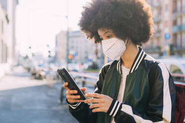 Young woman wearing protective face mask using mobile phone - MEUF02874