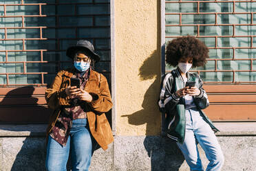 Multi-ethinc friends with protective face mask using smart phone on sunny day - MEUF02875