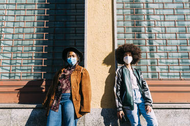 Junge Frauen mit Gesichtsschutzmasken stehen mit sozialer Distanz vor einem Gebäude - MEUF02882