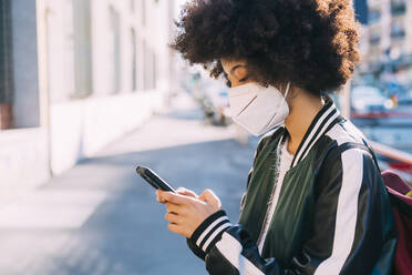 Woman wearing protective face mask using smart phone - MEUF02885