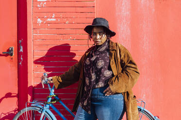 Young woman wearing hat standing by bicycle on sunny day - MEUF02895