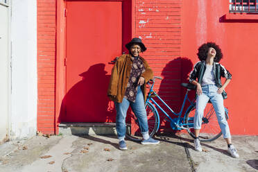 Glückliche Freundinnen stehen vor einem roten Gebäude an einem sonnigen Tag - MEUF02898