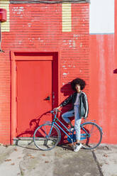 Junge Frau steht mit Fahrrad vor rotem Gebäude - MEUF02900