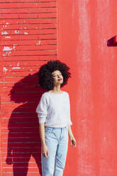 Afro hair woman day dreaming while standing in front of red wall - MEUF02927