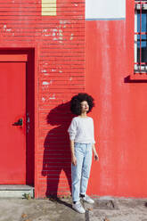 Thoughtful woman standing in front of red building - MEUF02928