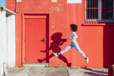 Young woman running by red building during sunny day - MEUF02934