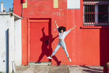 Young carefree woman jumping with arms outstretched on sunny day - MEUF02938