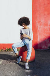 Junge Frau benutzt ein Mobiltelefon, während sie vor einer Wand sitzt - MEUF02951