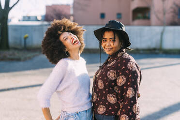 Young woman smiling while standing with cheerful friend on footpath - MEUF02957