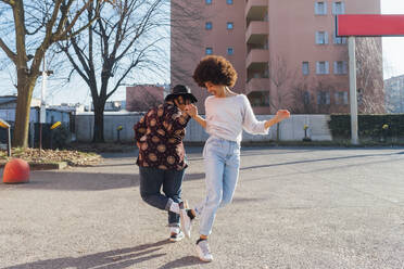 Cheerful women greeting through foot bumps on footpath - MEUF02961