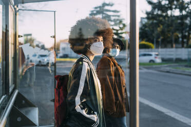 Freunde mit Gesichtsmaske warten am Busbahnhof bei Sonnenuntergang - MEUF02994