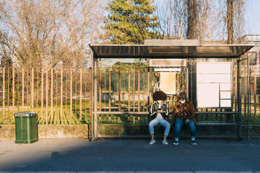 Freundinnen mit Gesichtsmaske beim Telefonieren am Busbahnhof - MEUF02995