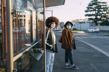 Junge Freundinnen mit Gesichtsmaske warten am Busbahnhof - MEUF02997