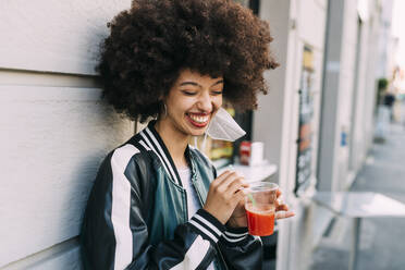 Cheerful woman with drink leaning on wall - MEUF03001