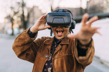 Fröhliche Frau, die ihre Hand ausstreckt, während sie einen Virtual-Reality-Simulator benutzt - MEUF03014
