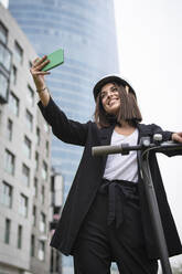 Unternehmerin mit elektrischem Tretroller, die ein Selfie über ihr Smartphone macht - SNF01449