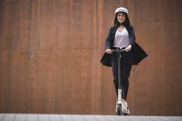 Female entrepreneur riding electric push scooter on footpath - SNF01456