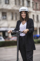 Businesswoman standing with electric push scooter - SNF01459