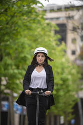Businesswoman with cycling helmet riding electric push scooter - SNF01463