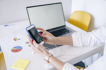 Woman using smart phone by laptop at home office - DGOF02228