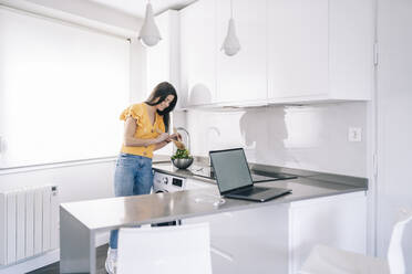 Frau bereitet Salat zu, während sie zu Hause an der Küchentheke steht - DGOF02230