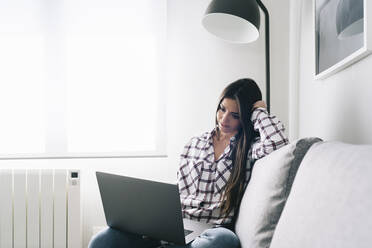 Frau benutzt Laptop, während sie zu Hause auf dem Sofa sitzt - DGOF02237