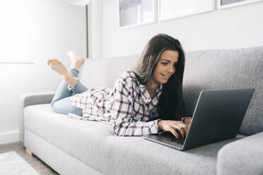 Young woman smiling while working on laptop in living room - DGOF02240