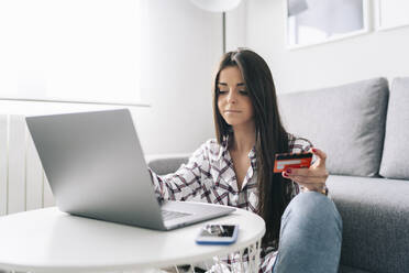 Woman with credit card paying online through laptop at home - DGOF02242