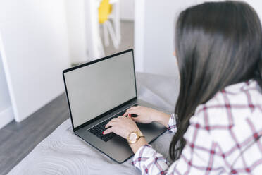 Junge Frau, die einen Laptop bei der Arbeit zu Hause benutzt - DGOF02254