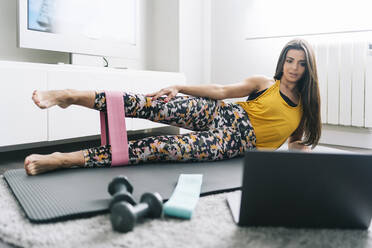 Woman doing home workout while learning through laptop in living room - DGOF02262